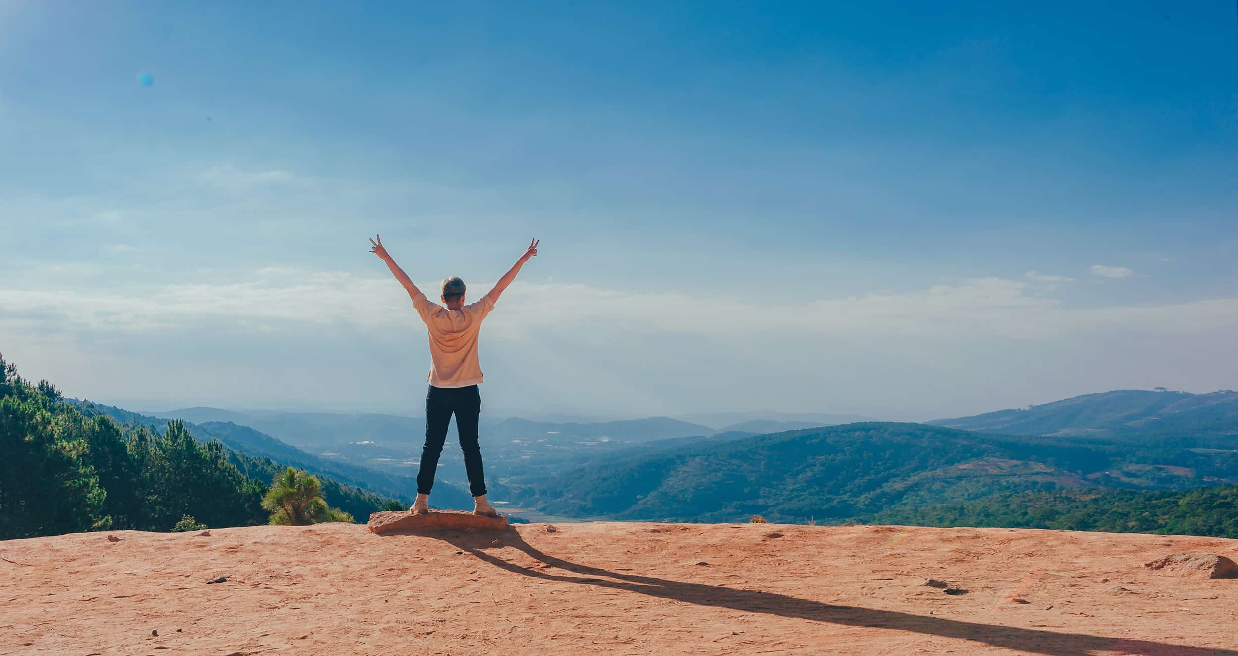 Person in Beige Top on Mountain Cliff Celebrating